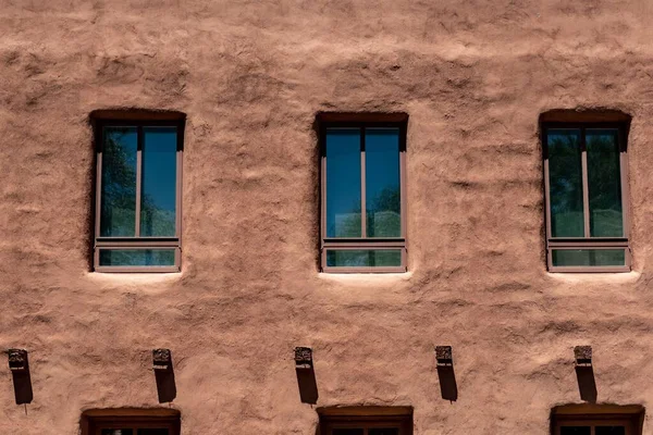 The facade of the brown wall of an adobe house and its windows
