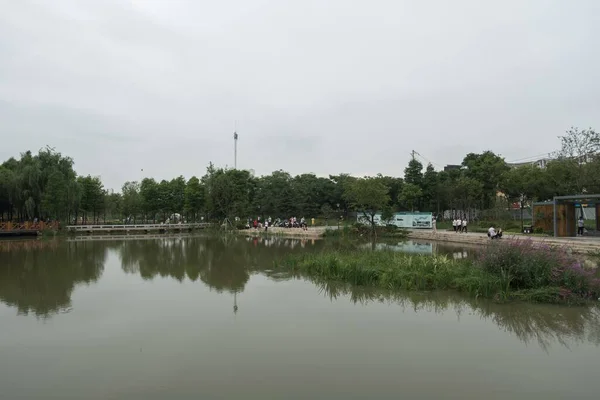 村子里的一个池塘静止不动 人们聚集在那里 在乌云密布的天空下参加一个公共活动 — 图库照片