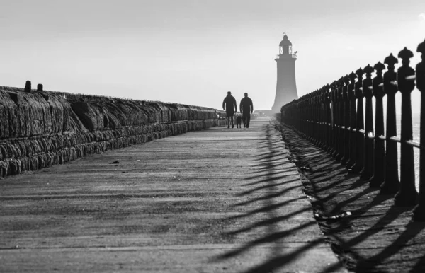 Szara Skala Sylwetek Spacerujących Molo Tynemouth Latarnią Morską Tle Wczesnym — Zdjęcie stockowe