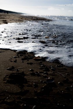 Siyah kum ve çakıl taşlarıyla sahile vuran deniz dalgalarının dikey görüntüsü..