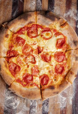 Ahşap tahtanın üzerinde un olan kalın kenarlı gurme pizzanın dikey üst görüntüsü.