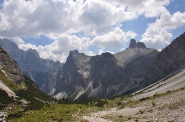 Mavi bulutlu gökyüzünün altında yeşil vadilerden ve kayalık tepelerden oluşan güzel bir manzara.