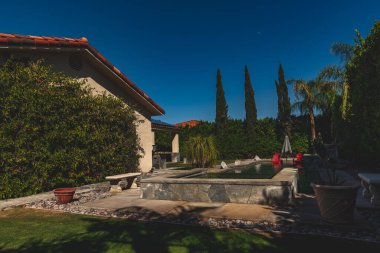 Güzel bir arka bahçesi ve mavi gökyüzünün altında havuzu olan bir evin yakın çekimi.