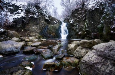 Karla kaplı kayalık kayalıklardan nehre düşen bir şelale.
