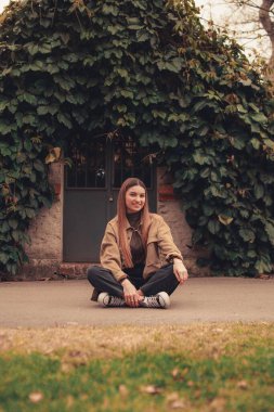 Tebessüm eden beyaz bir kadının çitin önünde otururken çekilmiş dikey bir fotoğrafı.