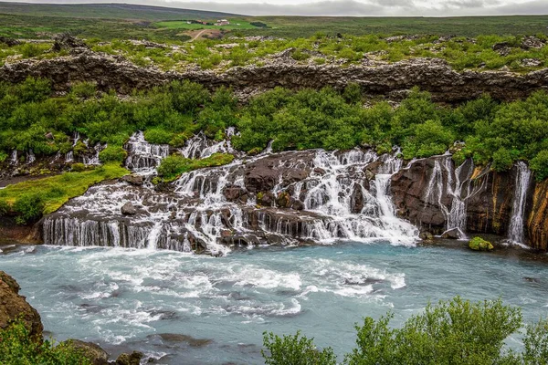 背景には緑豊かな木々があるアイスランドの岩の上を流れる美しい滝 — ストック写真