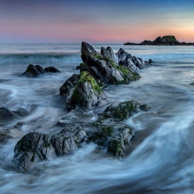 Gün batımında Long Strand, İrlanda yakınlarında denizdeki kayalar.
