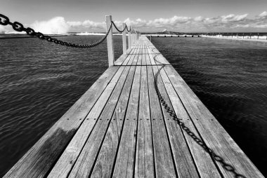 Zincirli uzun tahta bir iskelenin gri tonlu görüntüsü.