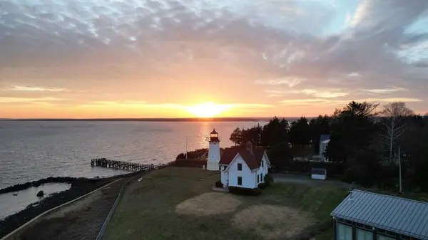 海岸沿いの家の隣にある灯台と海に沈む夕日のドローン — ストック写真