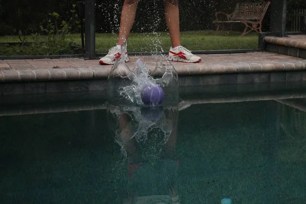 プールサイドに立っている人の足の後ろにプールの水にボールが飛び散る — ストック写真