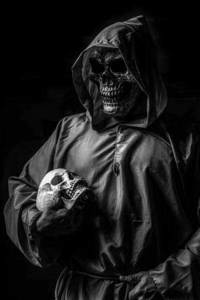 头盖骨 头盖骨一个戴头盖骨面罩的人拿着另一个在黑色背景上隔离的头盖骨的垂直灰度照片 — 图库照片