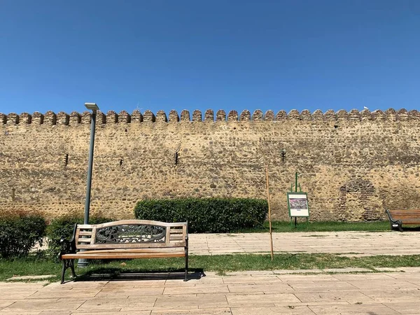 Güneşli bir günde Telavi, Georgia 'da duvarlarla çevrili bir kale boyunca boş bir ahşap bankın olduğu bir sokak.