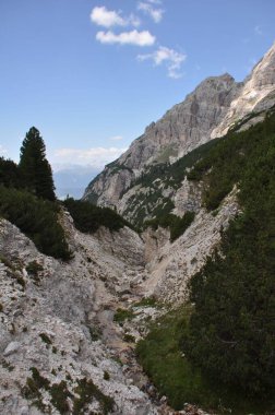 Mavi bulutlu gökyüzünün altında yeşil vadilerden ve kayalık tepelerden oluşan güzel bir manzara.