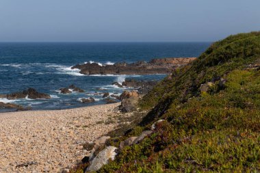 Arkaplanda kayalık dağlar ve su dalgalarıyla kaplı bir deniz kıyısı.