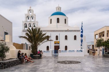 Oia, Santorini, Yunanistan 'da mavi kubbeli güzel beyaz bir kilisenin etrafında birçok insan var.