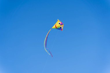 Yüzü açık mavi gökyüzüne uçan renkli bir uçurtma..