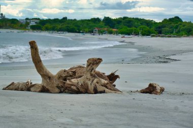 Bulutlu bir günde arka planda kayalık dağların olduğu bir deniz plajı.