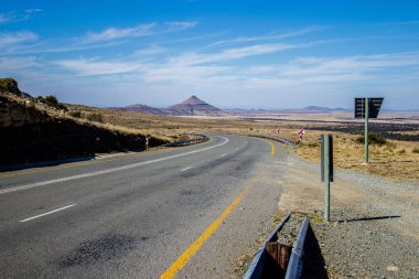 Gündüz vakti arka planda dağ zirveleri olan kırsal bir yolun manzarası.