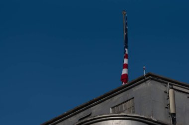 Endüstriyel bir binanın çatısında açık mavi gökyüzüne karşı bir Amerikan bayrağının alçak açılı görüntüsü.