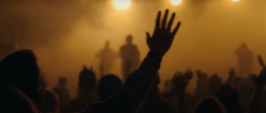 Bulanık bir arka planı olan büyük bir etkinlikte kaldırılan ellerin silueti.