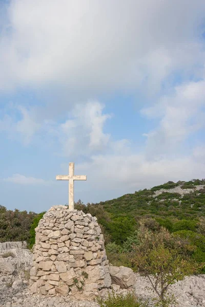 背景に緑豊かな木々の白い石の山の上に十字架の垂直ショット — ストック写真