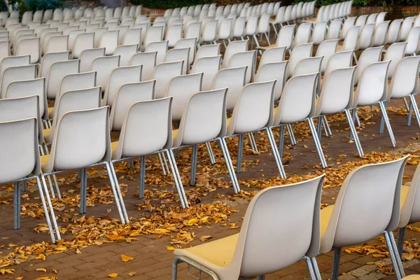 公园外面的一个公园 有一排白色的塑料椅子 铺着黄色的落叶 — 图库照片