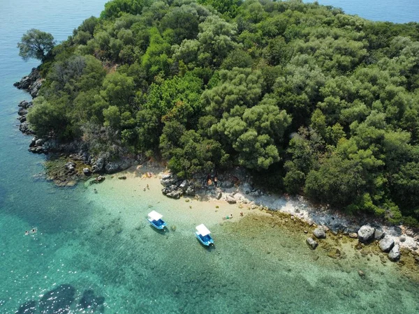 青い瀬に囲まれた多くの木がある島の海岸に停められたボートの空中ショット — ストック写真