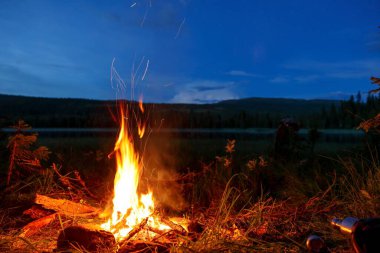 Gece İskandinav dağlarında bir gölün kenarında yanan bir kamp ateşine yakın çekim.