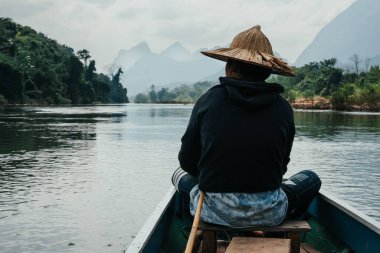 Nong Khiaw, Laos Dağları 'ndaki Nam Ou Nehri' ndeki teknede hasır şapkalı Asyalı çocuk.