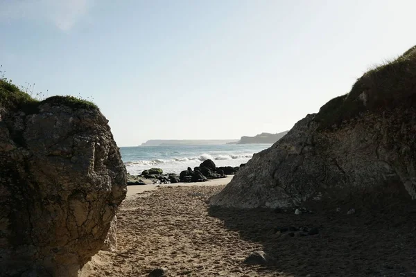 海岸線の中の砂の道澄んだ空の下で岩のビーチにつながる巨大な岩 — ストック写真