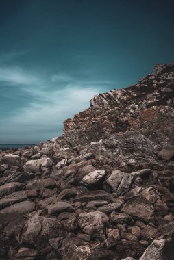 Bulutlu gökyüzüne karşı kayalık bir yamacın dikey dramatik görüntüsü.
