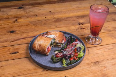 Lezzetli bir sandviçin yakın çekimi, yanında salata ve restoranın masasında serinletici bir içecek.