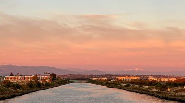 Güneş Los Angeles 'ta sahilde batıyor. Arka planda karla kaplı dağlar var.