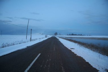 Soğuk ve sisli bir kış gününde iki yol kenarında boş bir yol ve kar.