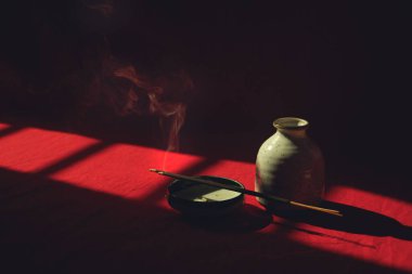 Tütsü çubuklarından yükselen duman gölgelerde saklı bir porselen tabakta meditasyon, farkındalık ve zihinsel refah kavramını gösteriyor.