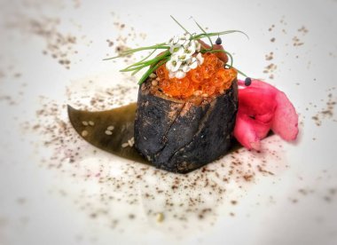 Kırmızı havyarla kaplanmış bir suşi rulosu ve tabakta garnitür.