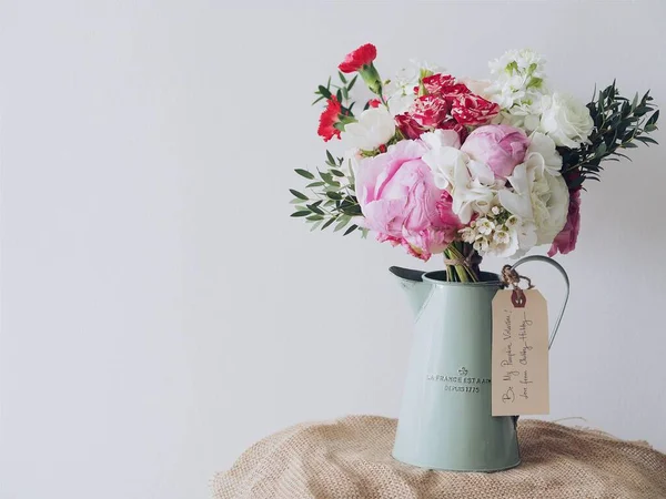 A closeup shot of a flower bouquet in a vintage watering can, with a white wall in the background, the concept of a romantic Valentine's Day