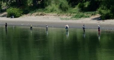 Sacramento nehrinin setinde balık avlamak için sıraya girmiş balıkçıların geniş bir görüntüsü.