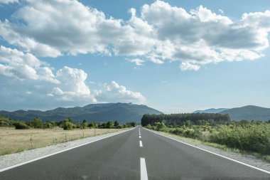 Açık arazi yolu manzarası, parlak mavi bir gökyüzü ve arka planda dağlar.