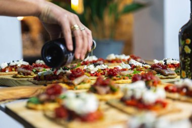 Ahşap bir tabakta aperatiflere yağ ekleyen bir kadın elinin yakın çekimi.