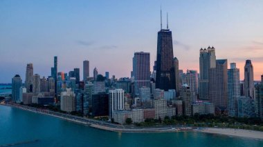 Gün batımında berrak gökyüzünün altında yüksek binalar olan güzel bir şehir manzarası.