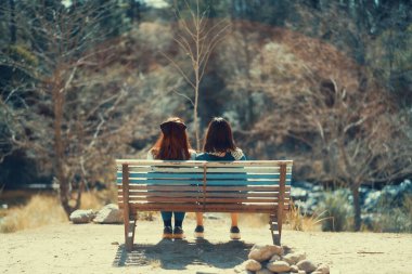 Parktaki bankta oturan iki kadının arka görüntüsü.