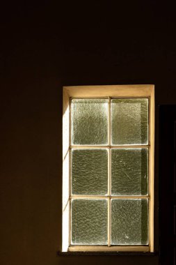 Koyu kahverengi bir duvar ve desenli camlı eski bir pencere..