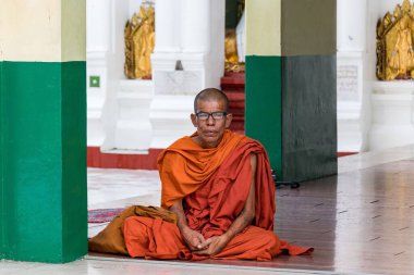 Tratizionell kırmızı cüppeli bir Budist keşişin portresi bir tapınakta yerde oturuyor.