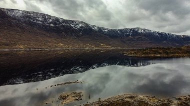 Kasvetli bir göl kıyısında, karlı dağların büyüleyici manzarası.