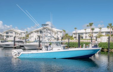 A horizontal shot of a blue boat at Ocean Reef Club with white seaside houses and nature in the background clipart