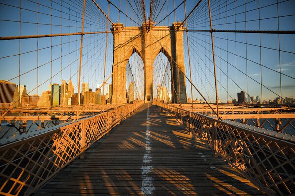 A daytime view of the Brooklyn bridge in the early morning with sunshine on it in New York