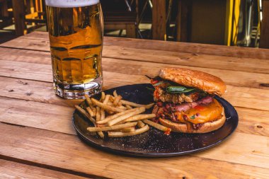 Lezzetli çıtır tavuk burger ve patates kızartması tabakta, ferahlatıcı bir bardak biranın yanında.