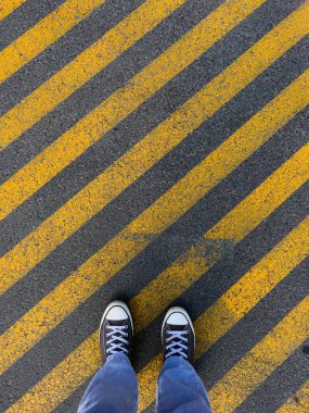 İşaretli asfalt zeminde duran birinin bacaklarının dikey üst görüntüsü