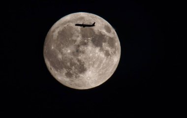 Karanlık gece gökyüzünde dolunaya karşı güzel bir uçak silueti görüntüsü.